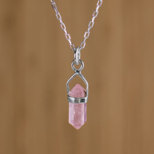 fondo plano de madera con imagen con zoom a colgante pequeño de piedra rosada con engaste de plata 925